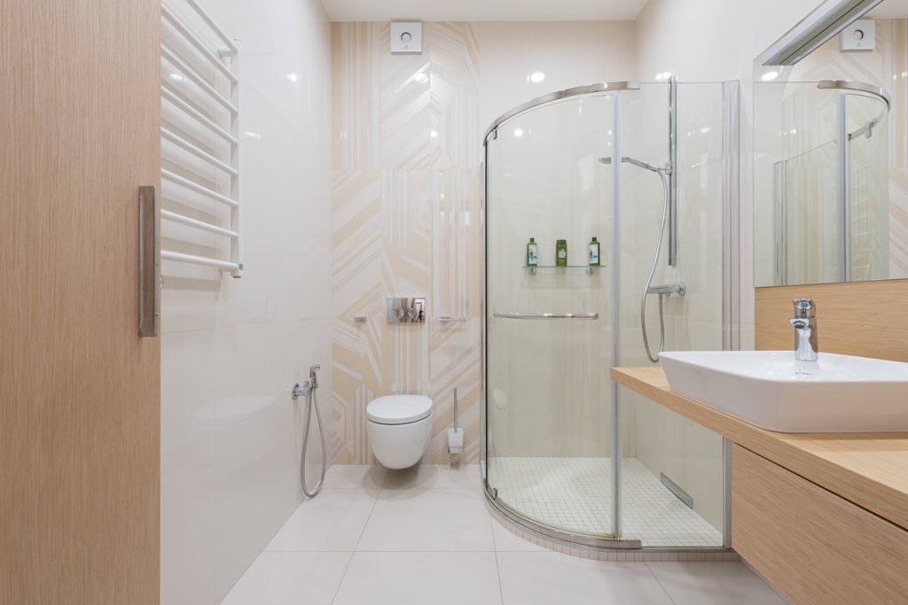 Interior of spacious light bathroom with shower cabin and wooden furniture